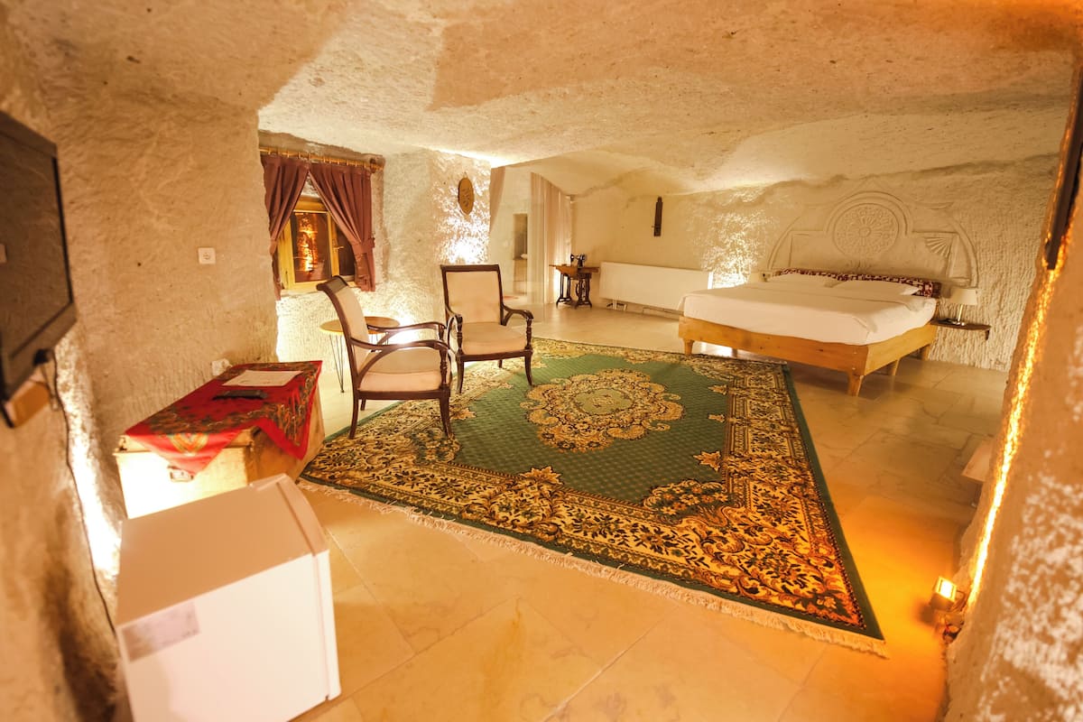 A bedroom with a large bed, two chairs, a table, and a patterned rug.