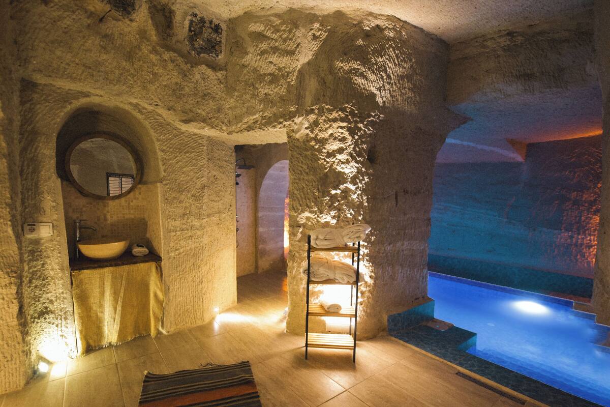 A spa room with a stone wall, a round mirror, a sink, a wooden bench, and a small pool.