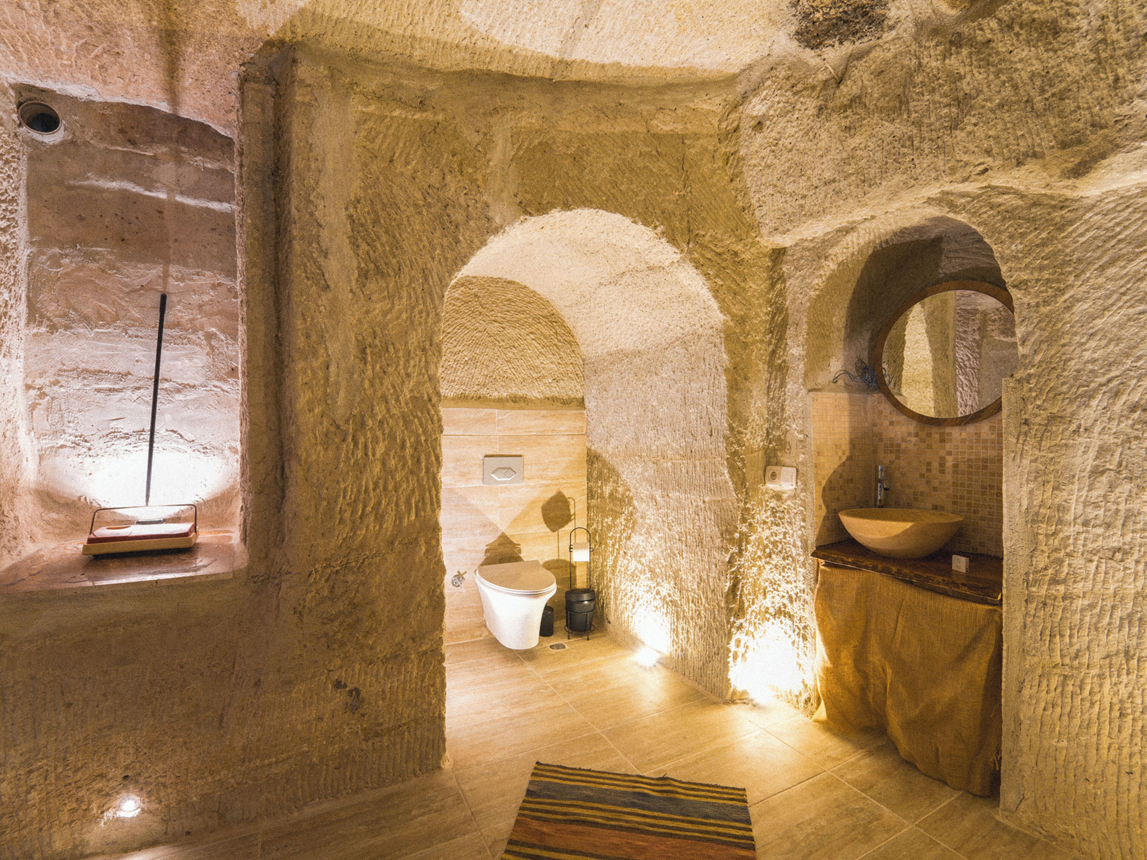 A stone-walled bathroom with a large sink, a mirror, and a toilet.