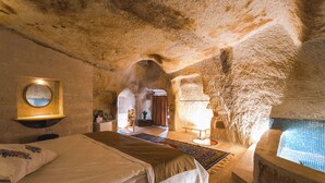 A room with a large bed, a smaller bed, a bathtub, and a mirror on the wall. - MY CAVE SUITE (Nevsehir)