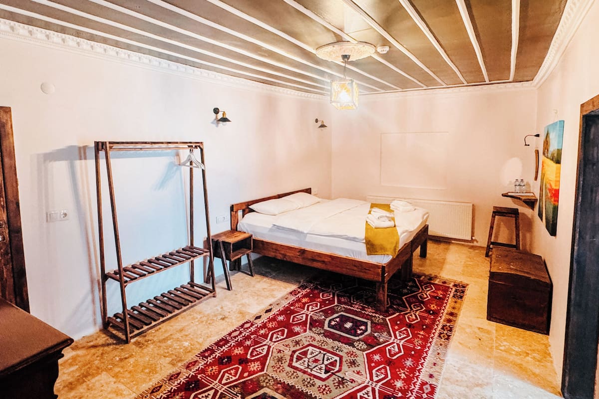 A room with a wooden bed, a metal wardrobe, a patterned rug, and a radiator.