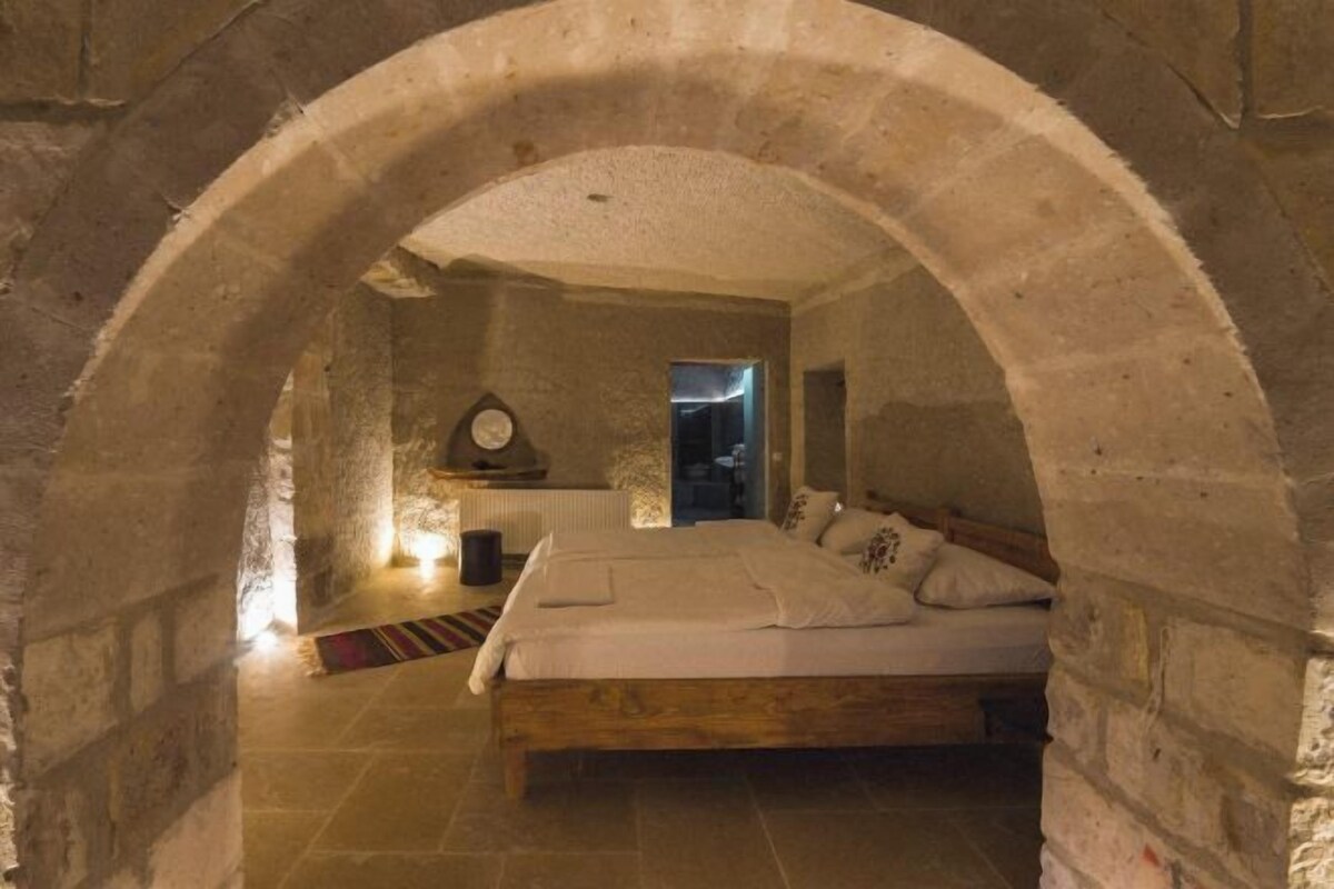 A bedroom with a stone archway, a wooden bed, a nightstand, and a radiator.