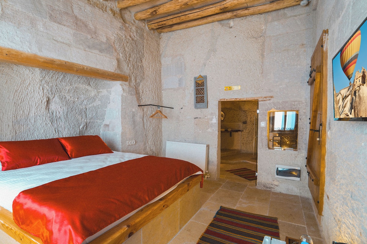 A bedroom with a wooden bed, a stone wall, a small bathroom, and a painting on the wall.