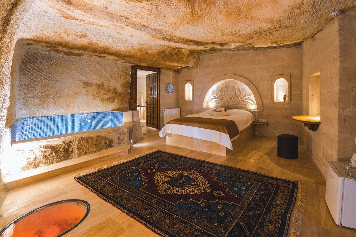 A bedroom with a large bed, a small window, a wall-mounted light, and a view of a blue-tiled pool.