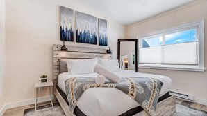 Een slaapkamer met een bed, nachtkastje, raam en wanddecoratie.