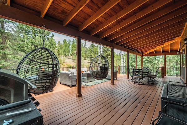 A covered outdoor deck with hanging chairs, a grill, and a table with chairs.