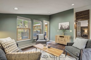 A cozy living room with a sofa, armchair, and coffee table. There is a wooden cabinet and a painting on the wall.