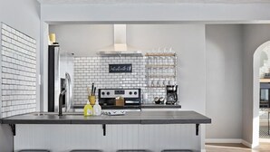 Uma cozinha moderna com ilha central, banquetas pretas, exaustor de aço inoxidável e um letreiro com a frase 'Just roll with it'.