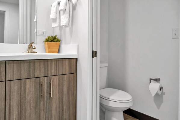 A modern bathroom with a wooden vanity, a white sink, a potted plant, and a toilet. - Garden-View Queen & Twin Suite | Condo at The Well Mouratoglou Academy | Tennis & Pickleball (Zephyrhills)