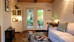 Ett mysigt rum med ett träpanelat tak, en vit soffa, ett litet bord med en lampa och en dörr som leder ut till en trädgård.