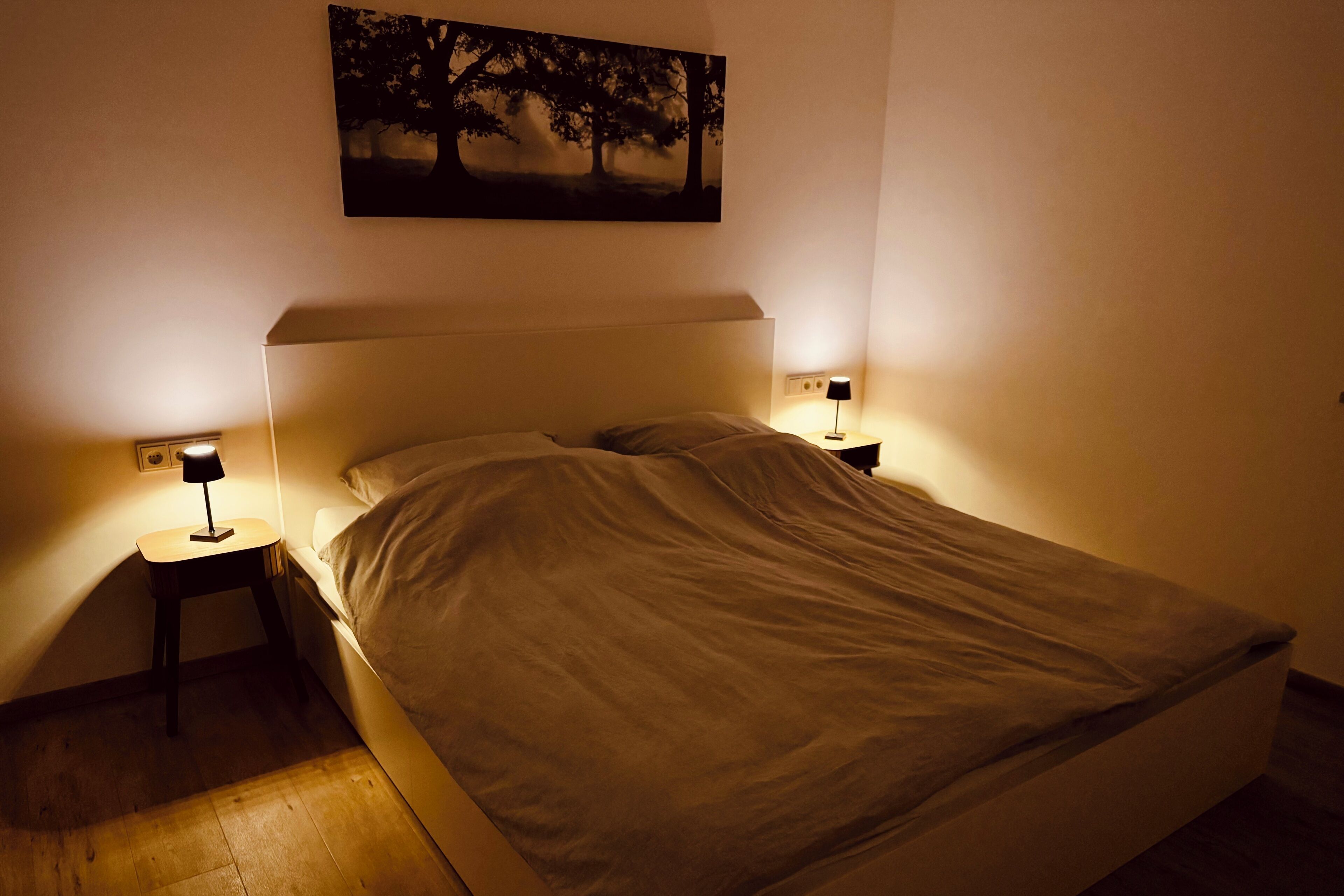 Quarto com cama, duas luminárias de cabeceira e um quadro na parede.