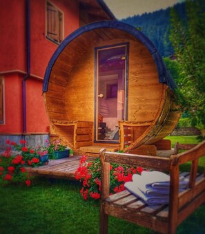 Una estructura de madera con forma de barril, con una puerta, dos sillas y una pequeña mesa en el exterior.