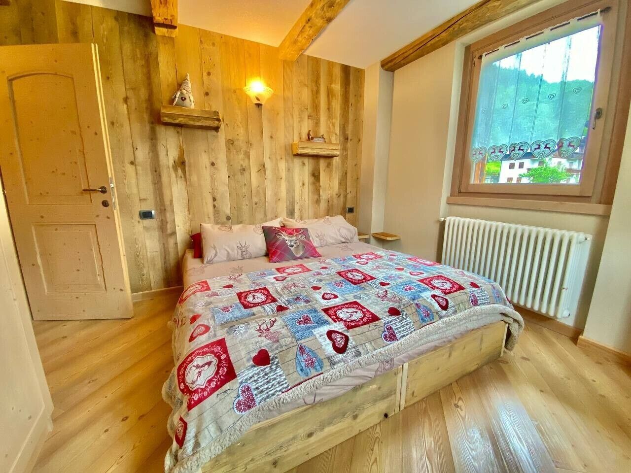 Ein Schlafzimmer mit Holzwand, einem Bett mit Steppdecke, einem Fenster mit Aussicht und einer Tür.