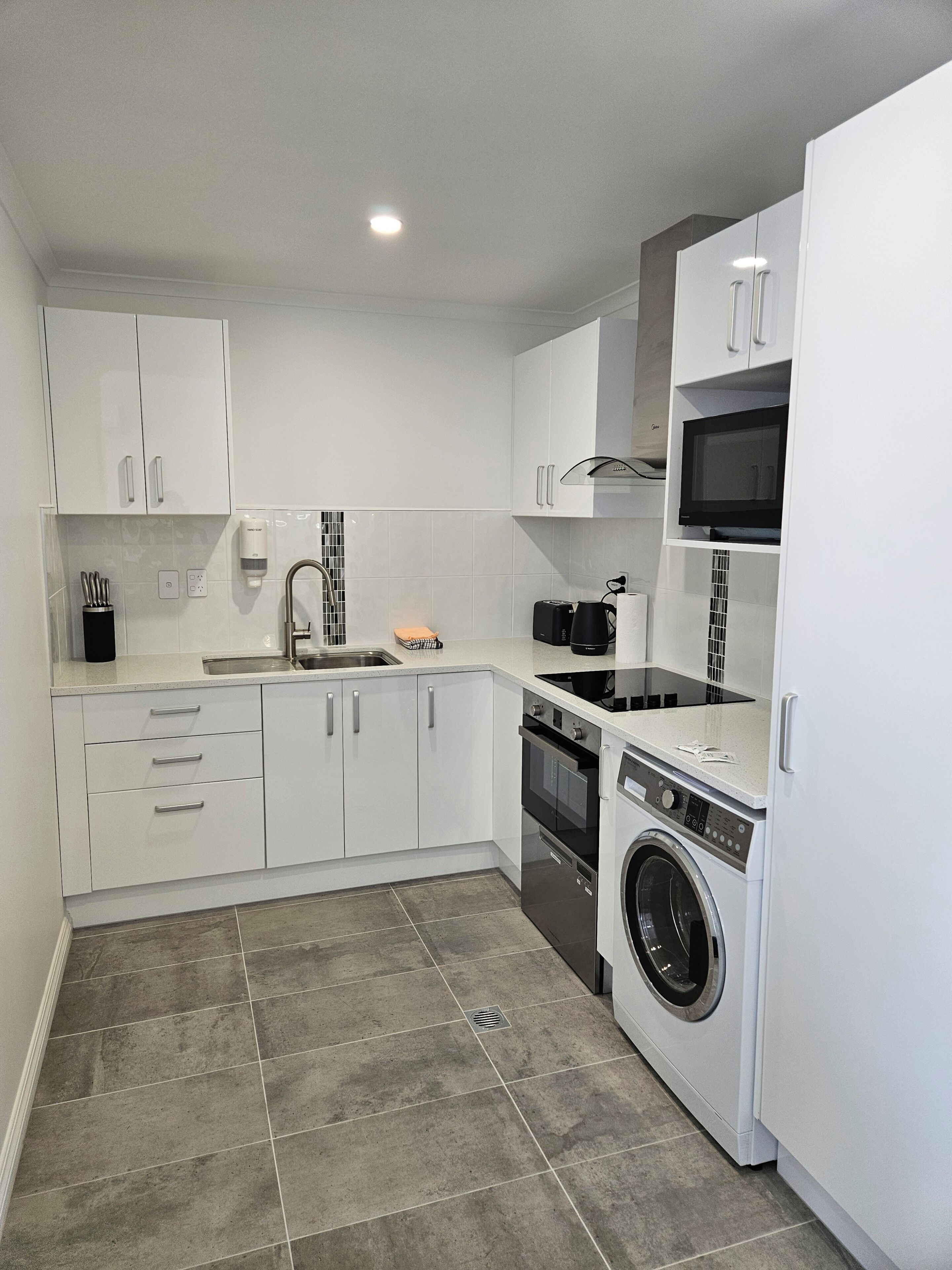 Une cuisine compacte avec des meubles blancs, un four à micro-ondes, une cuisinière et un lave-linge.