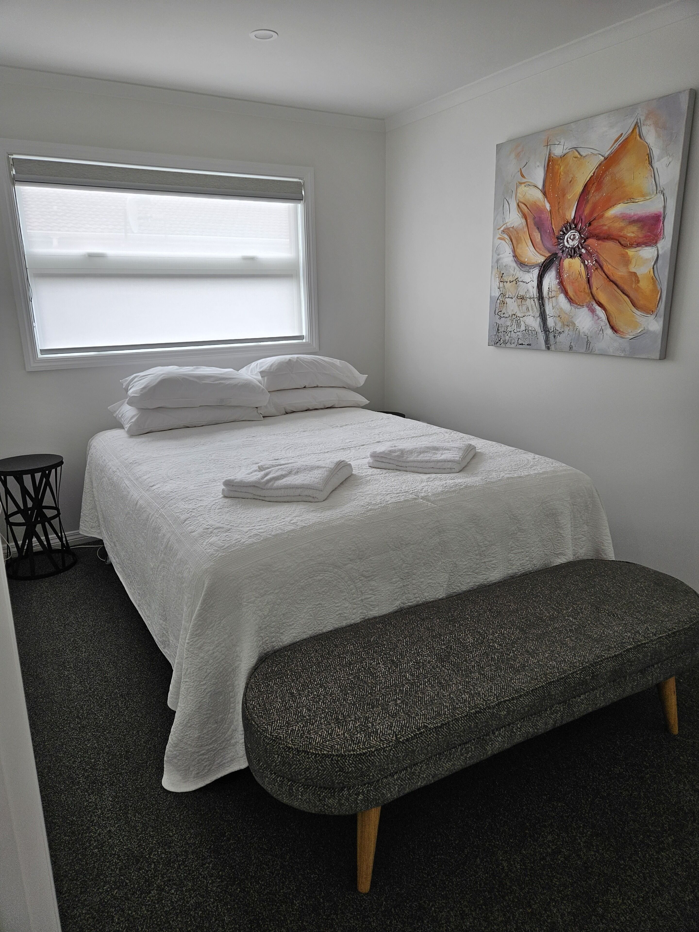 A bedroom with a bed, a bench, a window, and a painting.