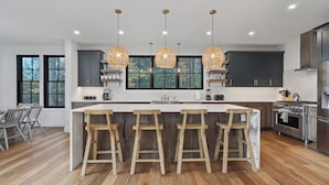 Een moderne keuken met een groot eiland, barkrukken, hanglampen en uitzicht op het buitenleven.