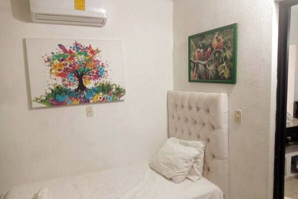 A bedroom with a white bed, a tufted headboard, and two paintings on the wall.