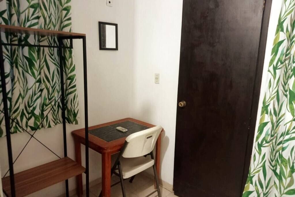 A small room with a wooden table and a white chair, a dark door, and a wall with a green leafy pattern.