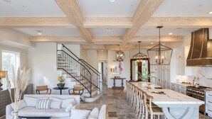 A spacious living area with a sofa, a coffee table, and a dining area with a large island and bar stools. A staircase leads to an upper level. - Sleeps 24, Elevator, Private Beach Boardwalk, Infinity Pool | 20 Bradley Circle (Hilton Head Island)
