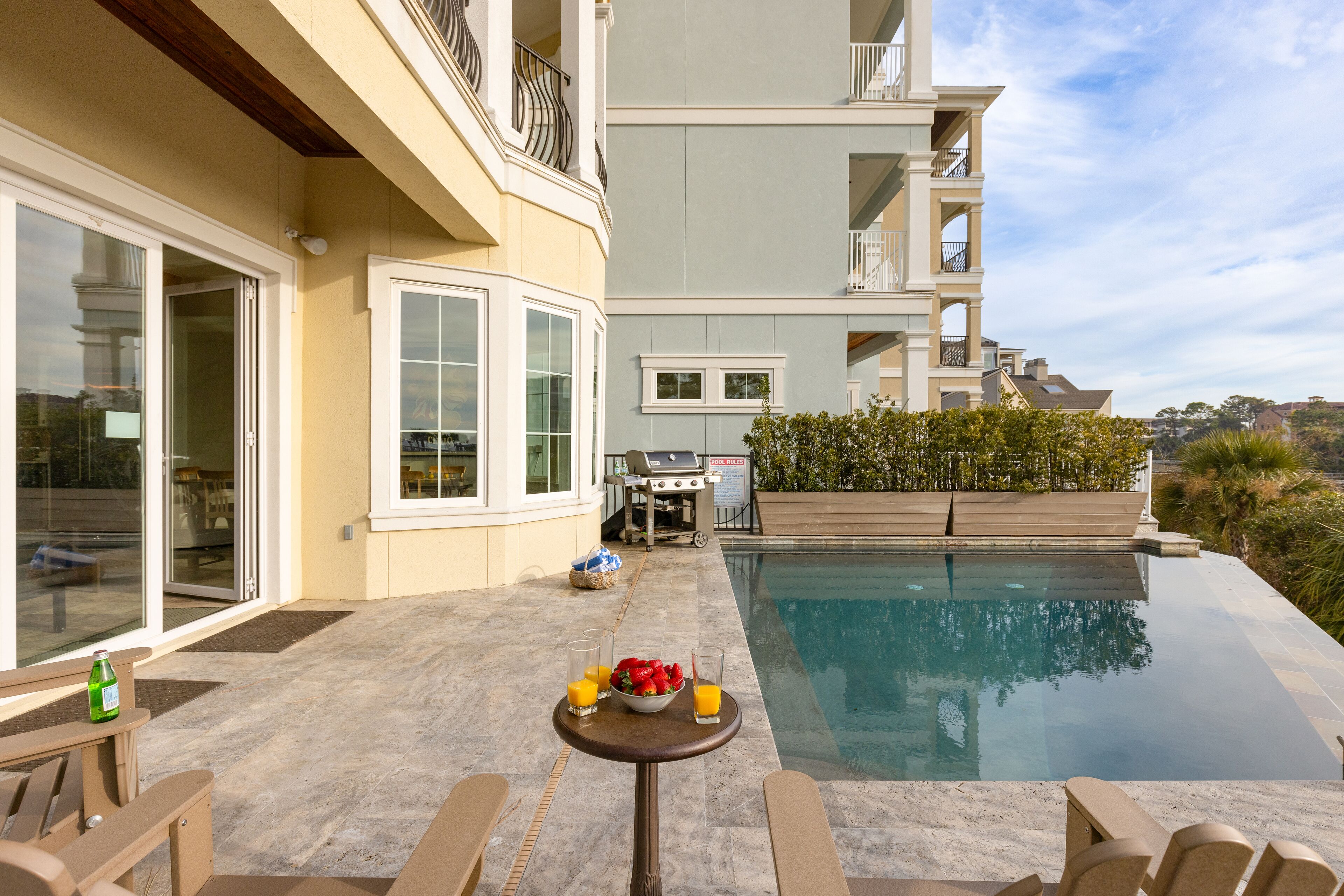 Un espace piscine avec une table pour deux, un barbecue et une vue sur un immeuble d’habitation.