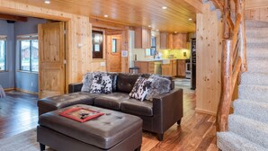Un vaste espace de vie comprenant un canapé d’angle en cuir, un plancher en bois et un escalier avec une rampe en bois.