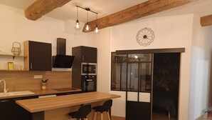 Eine moderne Küche mit einer Holzinsel, schwarzen Schränken und einem eingebauten Backofen. Zwei Barhocker und ein graues Sofa sind ebenfalls vorhanden.