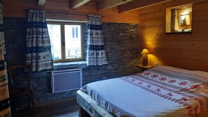 Een knus interieur met een stenen muur, een bed met een beddekleed met dessin, een raam met gordijnen en een lamp op een nachtkastje.
