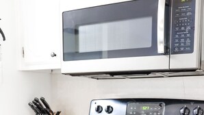 Una cocina con estufa negra, microondas encima y un juego de cuchillos en la encimera.