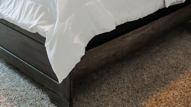 Una cama bien hecha con sábanas blancas, un cabecero oscuro y una planta verde a su lado.