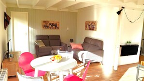 Una sala de estar con una mesa blanca, dos sofás y un televisor montado en la pared.