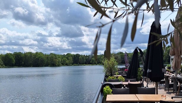 Un espacio al aire libre junto al lago con mesas y sillas, con vista a un lago tranquilo.