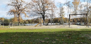 Explore a serene park setting with a playground featuring a swing set, slide, and bench, surrounded by trees and a body of water.