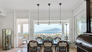 A dining area with a table set for four, a sofa, and a view of a cityscape and mountain. - La Quiete, Exclusive Villa with private pool and Jacuzzi (Vico Equense)
