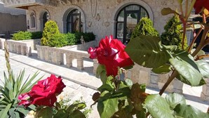A stone building with arched windows and balconies, surrounded by greenery and red flowers. - Cappadocia Chiaro (Nevsehir)