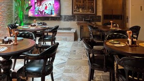 A restaurant with a brick wall, wooden ceiling beams, and a TV screen displaying a pink advertisement. - Cappadocia Chiaro (Nevsehir)