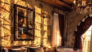 Une pièce avec un mur en pierre, un lit parsemé de pétales de rose, un lustre et une baignoire.