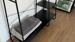 Ein schwarzes, offenes Regalsystem mit mehreren Ablagen, einer Leiter und einem Stapel gefalteter Handtücher.