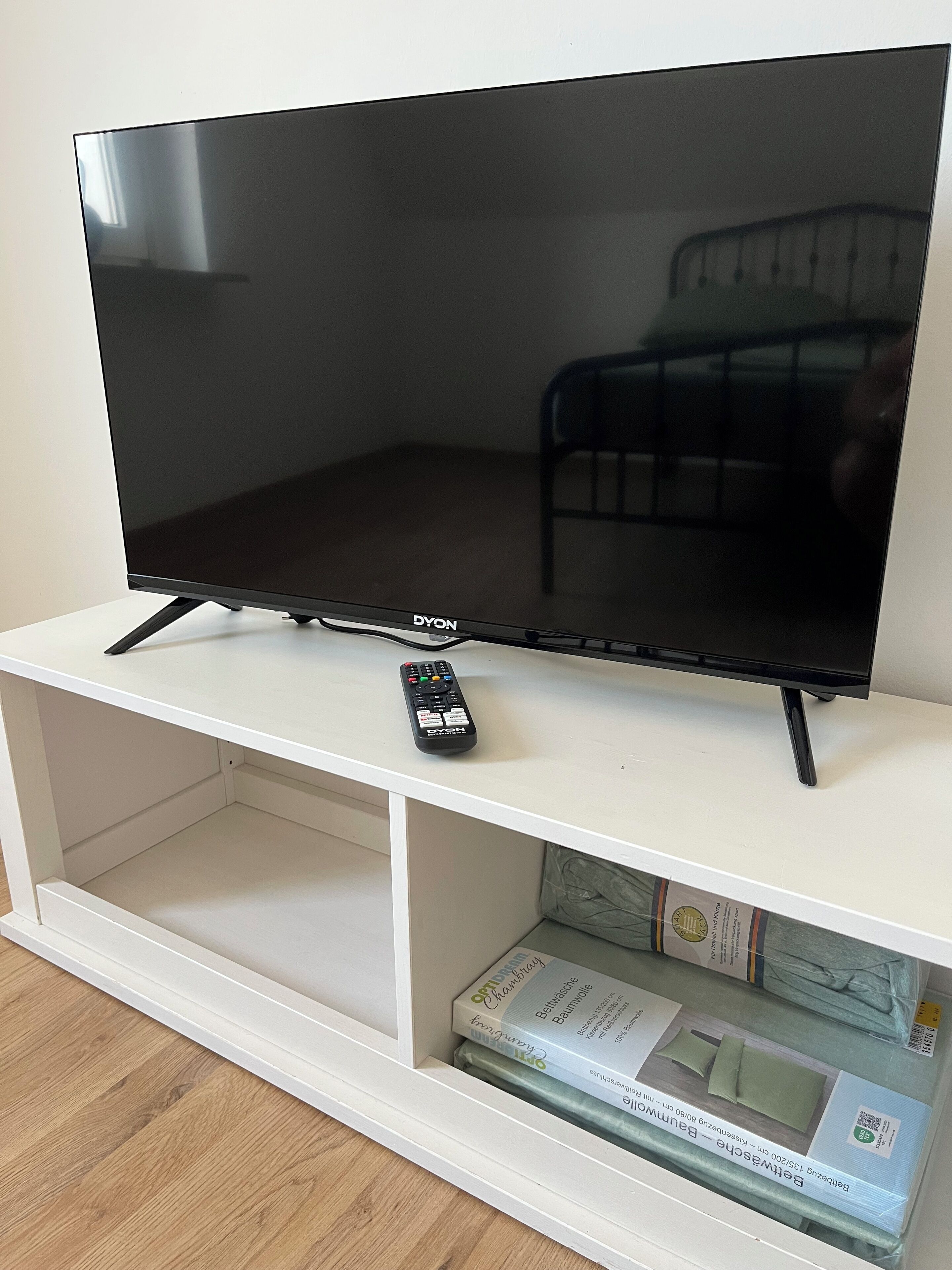 A flat-screen TV on a white stand with a remote control beside it.