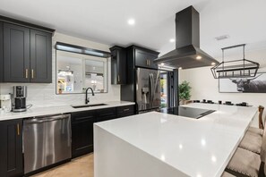 Una cucina moderna con mobili scuri, elettrodomestici in acciaio inossidabile, una grande isola e un lampadario.