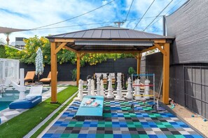 A backyard with a checkered floor, a pool, lounge chairs, and a gazebo.