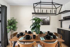 A dining area with a wooden table set for four, surrounded by chairs, a large potted plant, and a black pendant light. - 5ST Tranquil Escape in Vibrant Scottsdale (Scottsdale)