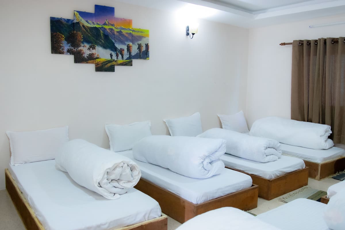 Ein Hotelzimmer mit vier Einzelbetten, alle mit weißen Laken und Kissen. Darüber an der Wand hängt ein Gemälde einer Berglandschaft.