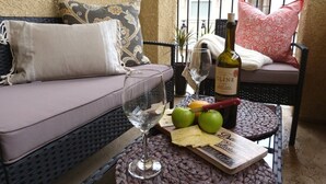 Un espace extérieur accueillant avec un canapé en osier, une petite table ronde et une bouteille de vin.