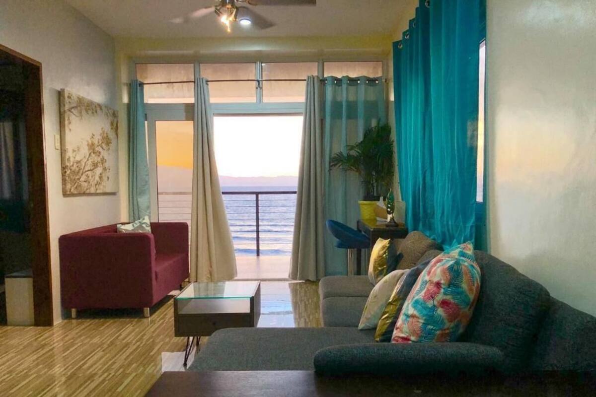 A living room with a sofa, a red armchair, a coffee table, and a view of the sea through large windows.