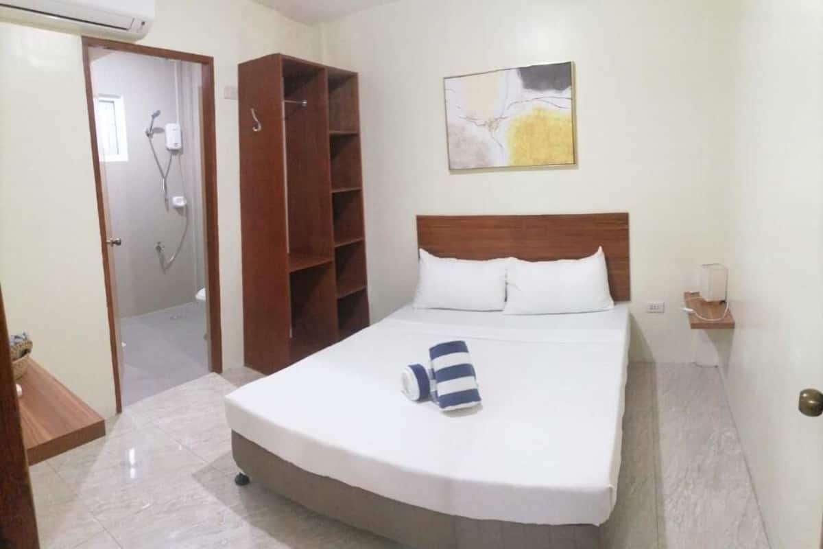 A hotel room with a bed, a wooden wardrobe, a shower area, and a painting on the wall.