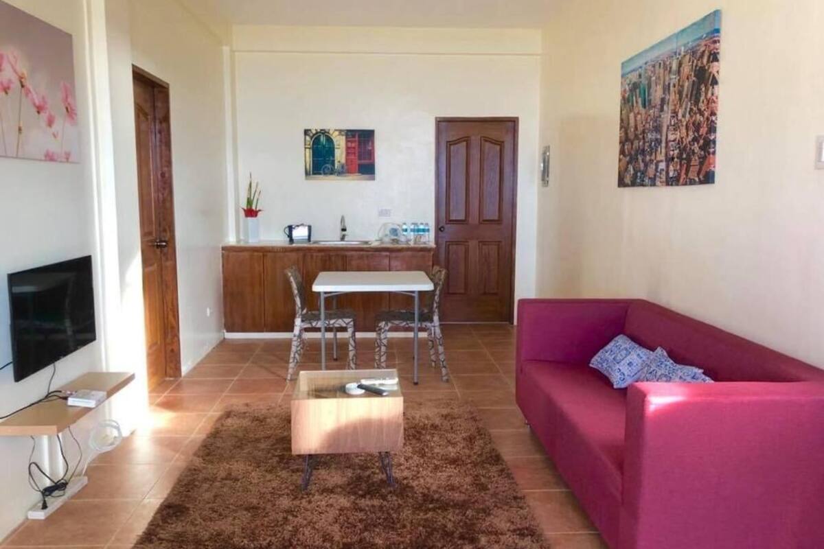 A living room with a red sofa, a coffee table, a TV, and a kitchen area with a dining table and chairs.