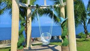 A gazebo with a swing chair, palm trees, and a view of the sea. - Acapulco Resort & Suites (Toledo City)