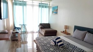 A hotel room with a bed, a sofa, a small table, a lamp, and a TV. - Acapulco Resort & Suites (Toledo City)