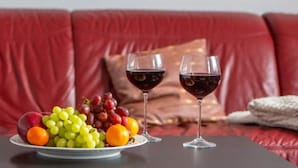 Ein rotes Ledersofa mit einer Obstschale und zwei Gläsern Rotwein auf einem Tisch.