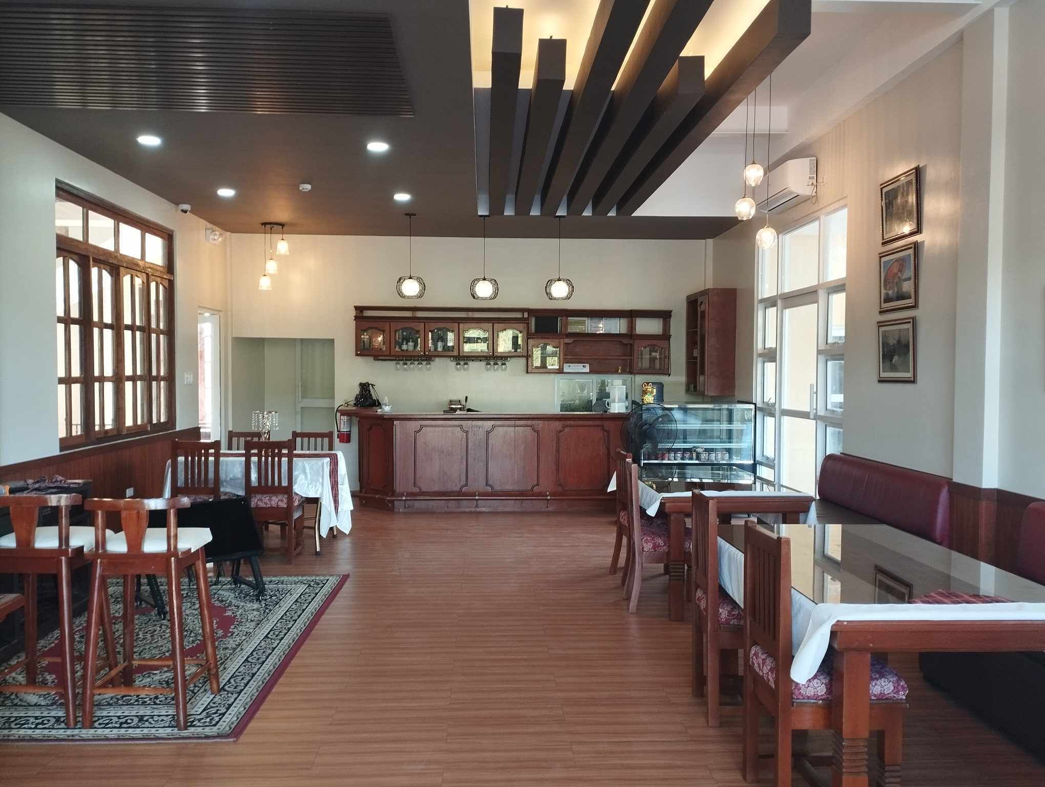 Un vaste espace dédié à la salle à manger, avec des meubles en bois, un bar central et une cuisine située au fond de la pièce.